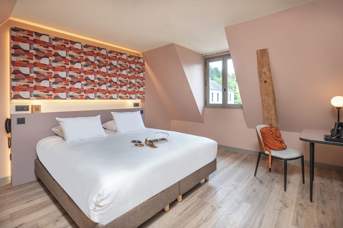 A modern hotel room with a large bed, a desk, and a chair.