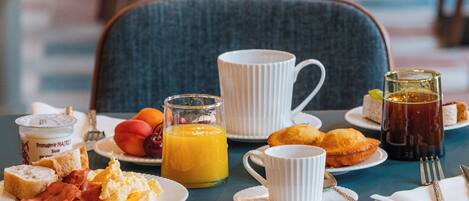 Une table de petit-déjeuner avec des assiettes remplies de nourriture, une carafe de jus d’orange, une tasse et un verre de thé.