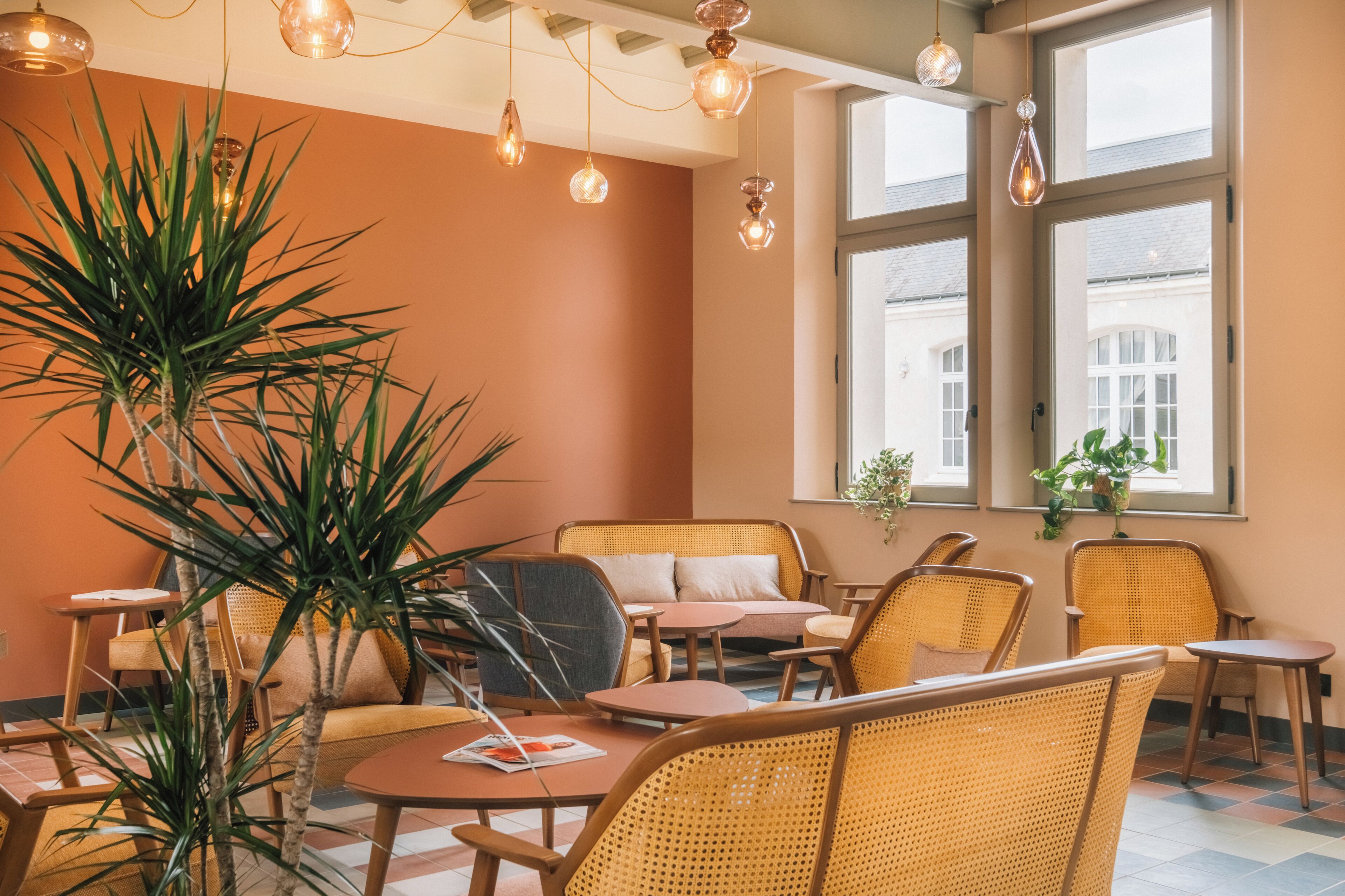 A cozy cafe with wicker furniture, large windows, and hanging pendant lights.