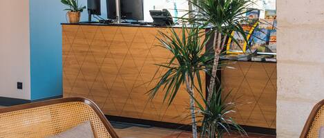 A reception area with a wooden counter, computer monitors, a potted plant, and wicker furniture.