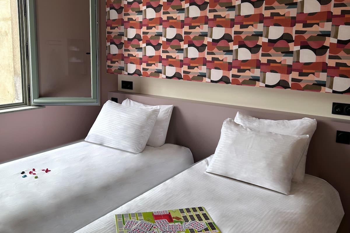 A hotel room with two beds, a patterned wall, and a window.