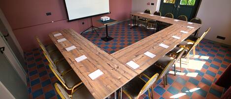 A conference room with a large wooden table, multiple chairs, a projector, and a screen.