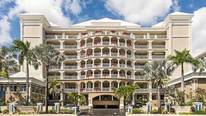 A multi-story hotel with a symmetrical facade, multiple balconies, and a central entrance. - Beachcomber 27 by Grand Cayman Villas (7 Mile Beach)