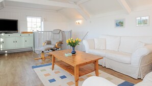 A spacious living room with a white sofa, a wooden coffee table, and a TV on a cabinet. - Manor Cottage Barn (Callington)
