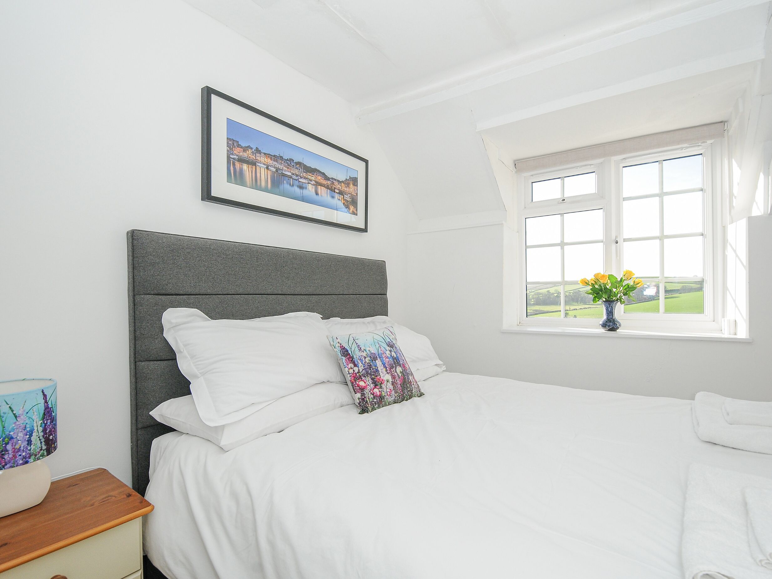 A neatly made bed with white linens, a grey headboard, and a framed picture above it.