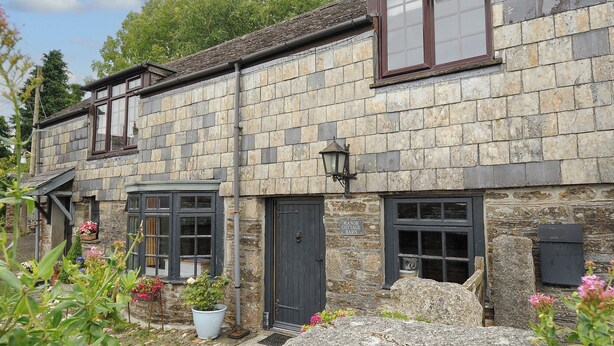 A stone cottage with a small garden, a black door, and a sign reading "Manor Cottage Barn". - Manor Cottage Barn (Callington)