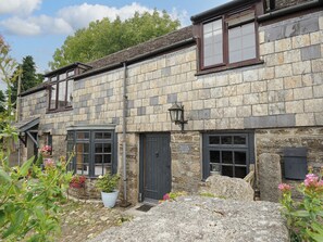 Una cabaña de piedra con un pequeño jardín, una puerta negra y un letrero que dice 'Manor Cottage Barn'.