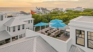 A rooftop terrace with outdoor furniture and umbrellas, overlooking a coastal area with houses and the sea. - Summer Nights|Easy Beach Access|Private PoolGolf Cart (Santa Rosa Beach)