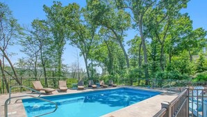 Ein rechteckiger Swimmingpool mit einer Metallleiter, umgeben von einer Betonplattform. Liegestühle und ein Zaun begrenzen das Areal.