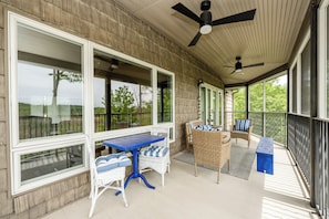 Une terrasse couverte, aménagée avec des meubles en osier, une table bleue et des ventilateurs de plafond.