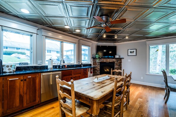 A spacious kitchen with a wooden dining table, a stone fireplace, and a ceiling fan.