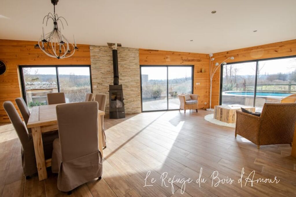 Una habitación amplia con una gran mesa de madera y sillas, una chimenea de piedra y ventanas grandes que ofrecen vistas al exterior.