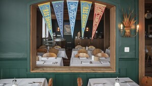 A restaurant interior with tables set for dining, a wooden archway, and hanging banners. - Drei Berge Hotel (Mürren)