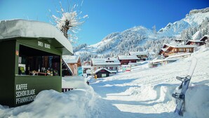 A snow-covered mountain village with a green building labeled "Drei Berge" and a snowboard leaning against a snow wall. - Drei Berge Hotel (Mürren)