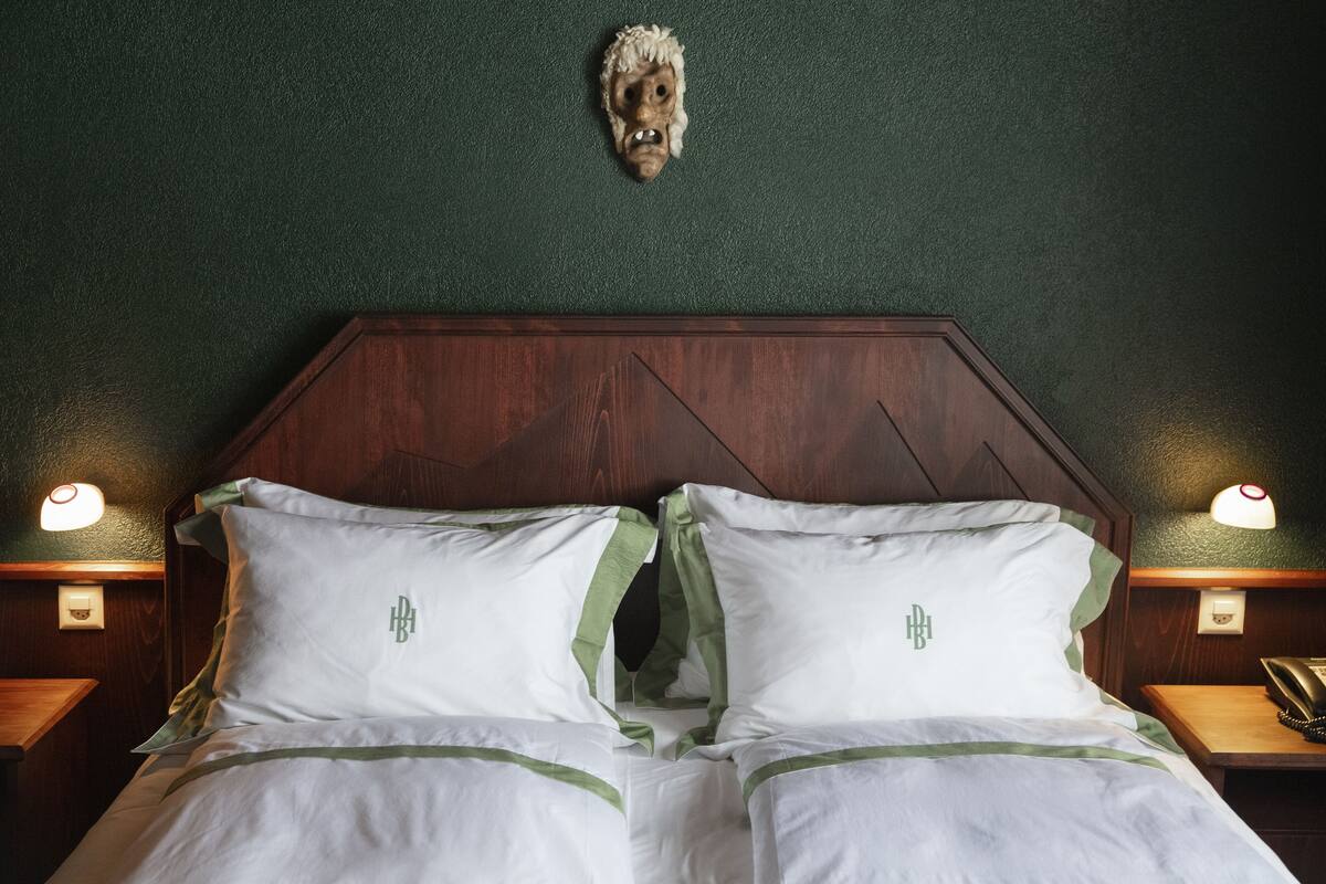 A hotel room with a wooden headboard, two white pillows with a green stripe, and a wall-mounted animal head.