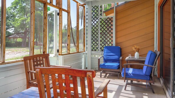 A covered porch with wooden chairs and a table, large windows, and a lattice screen. - Southern Daze I Walk to Jacob's Well & Morrow Park (Wimberley)