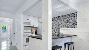 A modern kitchen with white cabinetry, a black countertop, and a patterned backsplash. There are two black stools at the counter. - Southern Daze I Walk to Jacob's Well & Morrow Park (Wimberley)