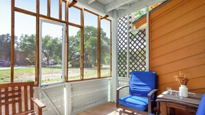 A covered porch with a wooden bench, a blue chair, and a table with a vase of dried flowers. - Southern Daze I Walk to Jacob's Well & Morrow Park (Wimberley)