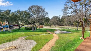 A well-maintained outdoor area with a gravel path, green grass, and trees. - Southern Daze I Walk to Jacob's Well & Morrow Park (Wimberley)