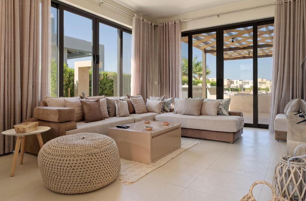 Un salon moderne comprenant un ensemble de canapés, un pouf, une table basse et une vue dégagée grâce à de grandes fenêtres.