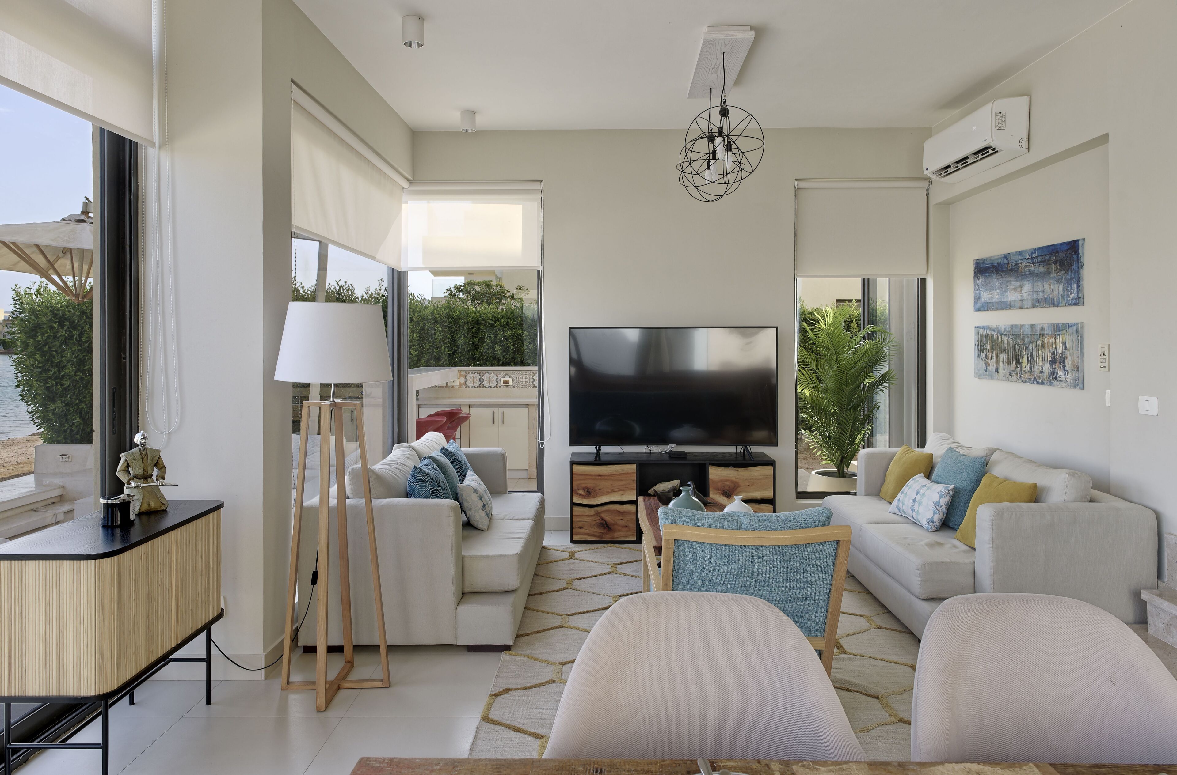 A modern living room with a large flat-screen TV, a sofa, a coffee table, and a desk with a lamp.