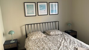 A bedroom with a bed, two nightstands, and three framed pictures on the wall. - (Menton)