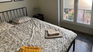 A bedroom with a bed, a window, and two framed pictures on the wall. - (Menton)