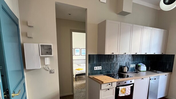 A modern kitchen with white cabinets, a black backsplash, and a red hexagonal floor pattern. - (Menton)