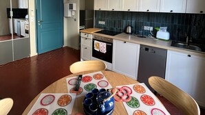 A modern kitchen with white cabinets, a blue door, and a wooden dining table with citrus fruit decorations. - (Menton)