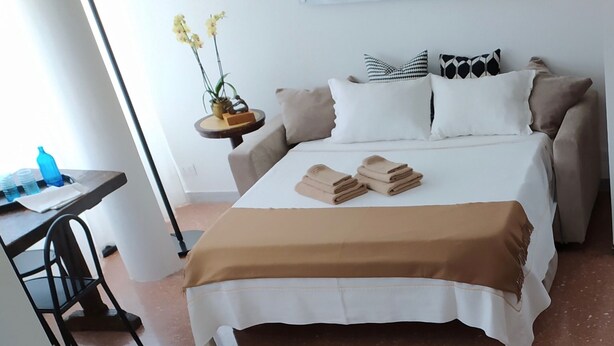 A neatly made bed with a brown blanket, a small table with a blue bottle, and a chair. - House St. Peter Rome (Roma)