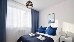 Een moderne hotelkamer met een groot bed, een nachtkastje en een raam met dunne gordijnen.