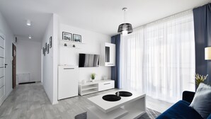 Een moderne woonkamer met een witte bank, een salontafel, een televisie en een eethoek met een wit kastje en een plant.