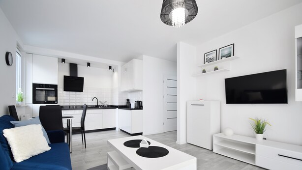 Een moderne woonkamer met een blauwe bank, een witte salontafel en een aan de muur bevestigde televisie.