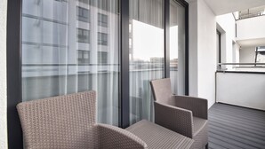 Een balkon met rieten stoelen, grote ramen met gordijnen en uitzicht op de stad.
