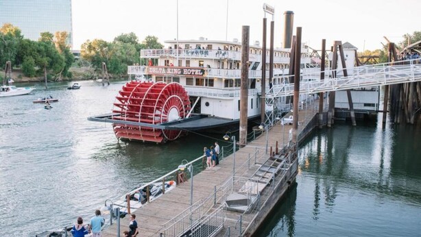 Un hôtel-paquebot avec une grande roue à aubes, amarré à un quai où des gens se promènent.