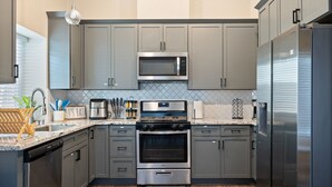 Une cuisine moderne avec des meubles gris, des appareils en acier inoxydable, un four encastré et un four à micro-ondes.