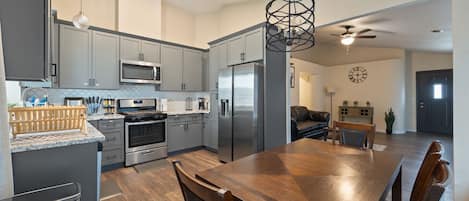 A modern kitchen with grey cabinets, stainless steel appliances, and a wooden dining table.