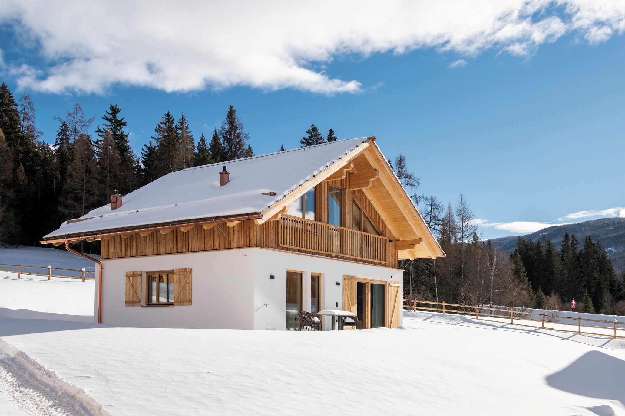 Eine Holz-Blockhütte mit Balkon, Essbereich und Blick auf eine verschneite Landschaft mit Bäumen und Bergen.