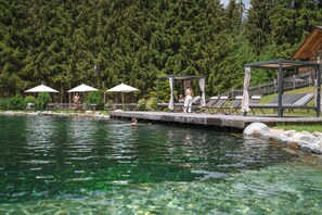 A swimming pool with lounge chairs and umbrellas, surrounded by a wooden deck and a forested area. - Lerchpeuntgut (Tamsweg)