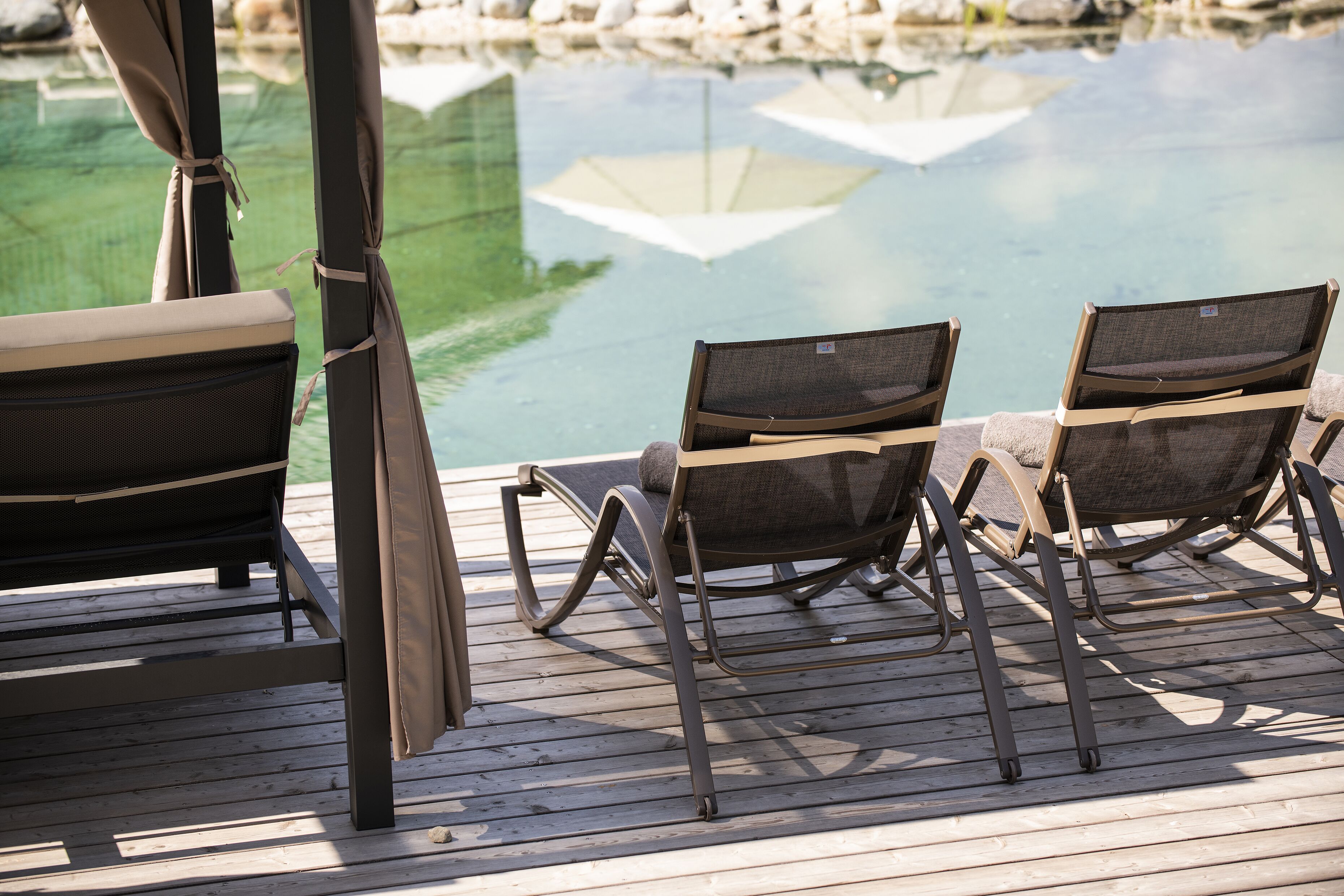 Terraza de madera con dos sillones de descanso frente a una piscina.