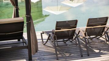 Terraza de madera con dos sillones de descanso frente a una piscina.