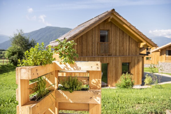 A wooden bench with planters in a grassy area with a wooden building in the background.