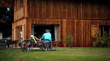 Ein Holzhaus mit großem offenen Durchgang, einem Fahrrad davor und einer Person, die auf einer Bank sitzt.