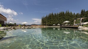 Una piscina cristalina con sillas de descanso y sombrillas, rodeada de árboles y un edificio.