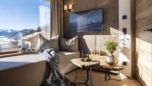 Una sala de estar moderna con un televisor grande, un sofá acogedor, una mesita con un florero y vistas a la montaña.