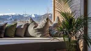 Asiento junto a la ventana con cojines, una planta en maceta y vistas a montañas nevadas.