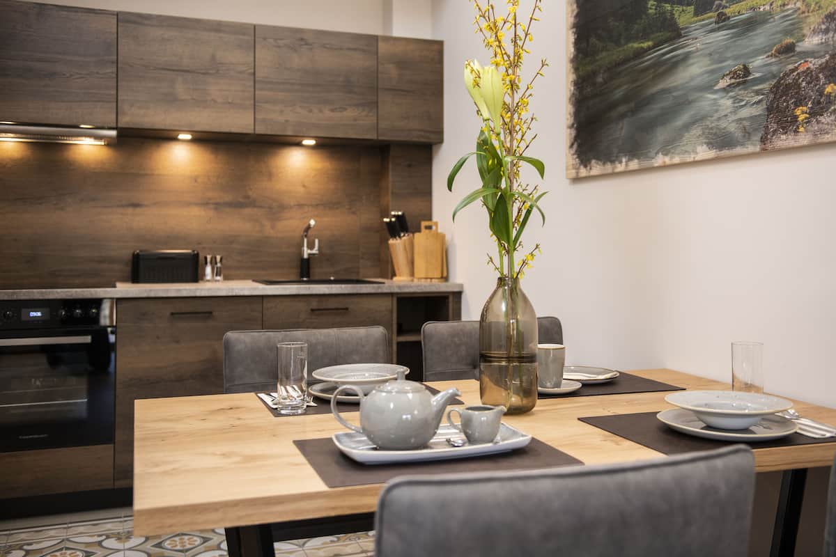 A modern kitchen with wooden cabinets, a dining table set with plates, a teapot, and a vase with flowers.