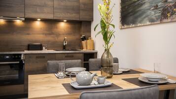 A modern kitchen with wooden cabinets, a dining table set with plates, a teapot, and a vase with flowers.