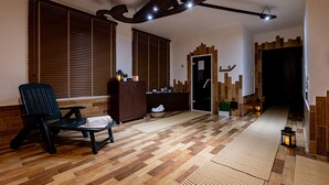 A spacious room with a wooden floor, a dark-colored chair, a small table, and a cabinet. There is a door leading to another room, and a wall with a unique pattern. - Penzión Lomnicky (Stara Lesna)