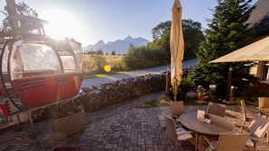A patio area with a round table and chairs, a cable car in the background, and a mountain view. - Penzión Lomnicky (Stara Lesna)